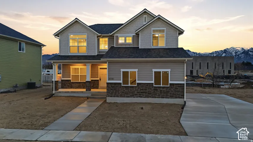 Two-story residence featuring a covered front porch, stone and siding exterior, multiple window styles, and an attached driveway