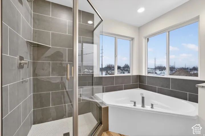 Walk-in shower with tile surround and glass enclosure, separate soaking tub with tile surround, and multiple windows