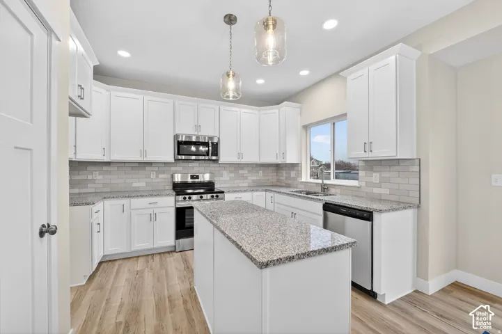Kitchen featuring white cabinetry, light-toned wood-finish flooring, stainless steel appliances, a center island, and pendant lighting