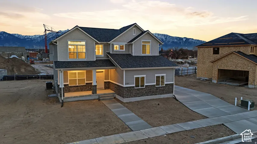 Two-story exterior with light gray siding and stone accents, featuring a covered porch with white columns and a gray shingle roof