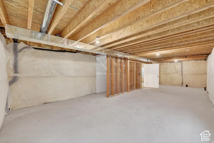 Exposed wood joists, concrete flooring, recessed lighting, framed wall sections, and a solid panel door