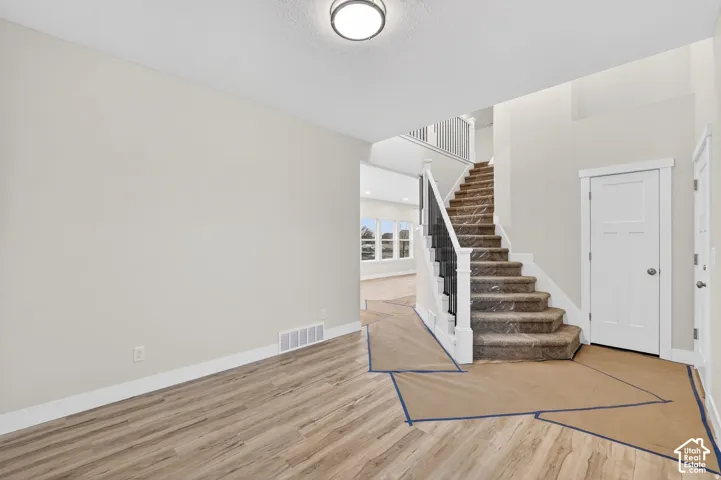 Wood-finish flooring, recessed ceiling lighting, and a staircase with white risers and dark balusters