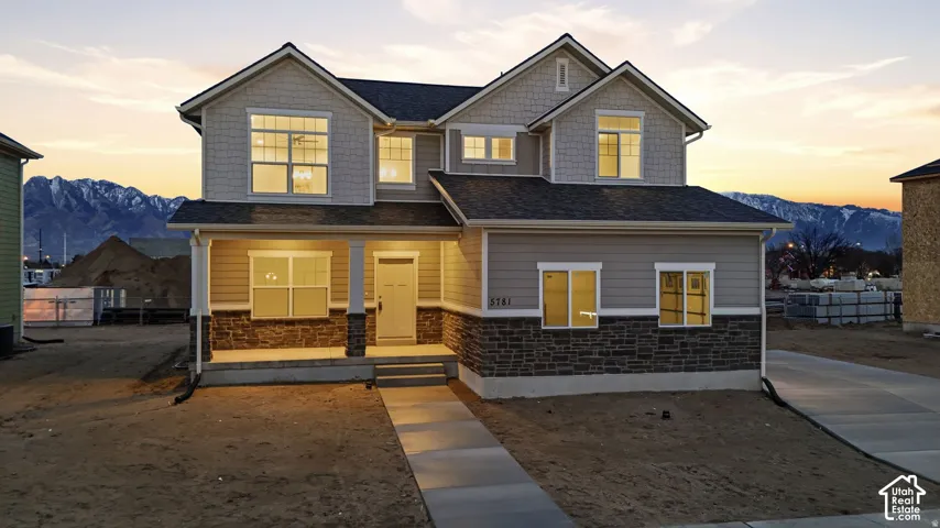 Two-story residence featuring a covered front porch with columns, a stone and siding exterior, a concrete walkway, and a paved driveway