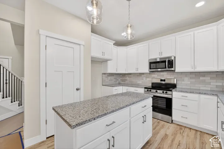 White shaker cabinetry with brushed nickel hardware, stainless steel appliances, a kitchen island with a stone countertop, a subway tile backsplash, and wood-finish flooring