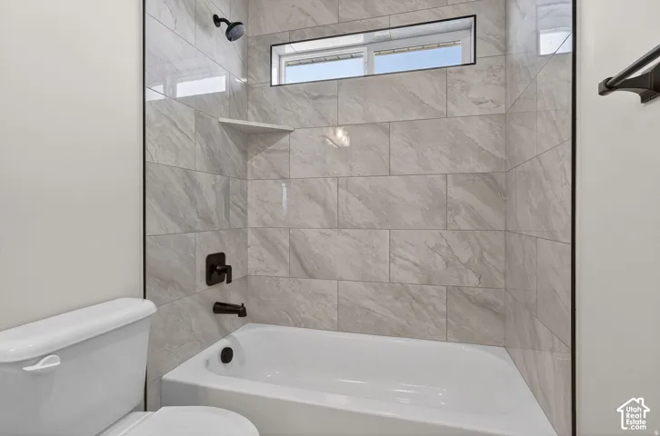 Bathtub with gray tiled surround, integrated corner shelf, horizontal transom window, and matte black fixtures