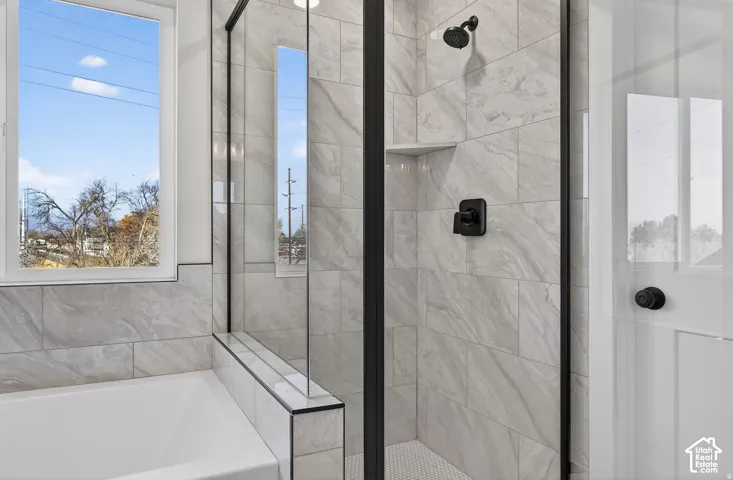 Shower with clear glass enclosure and matte black fixtures, integrated shelving, and white hexagonal tile flooring