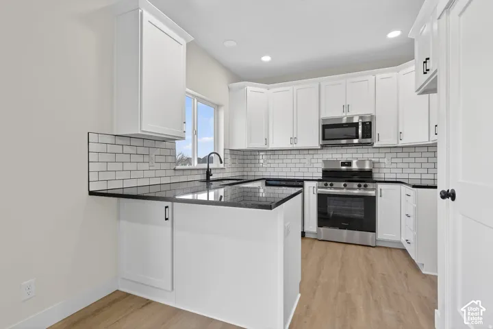 White cabinetry with matte black hardware, black countertops, subway tile backsplash, stainless steel appliances, and wood-finish flooring