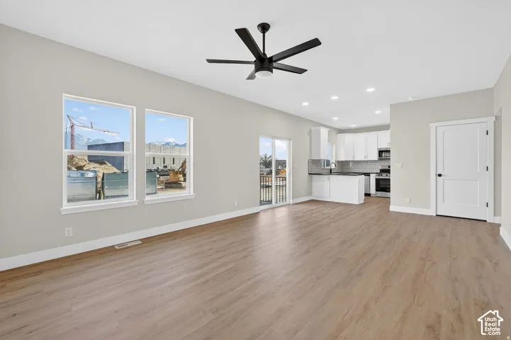 Open concept living area with wood-finish flooring, two windows, and a ceiling fan