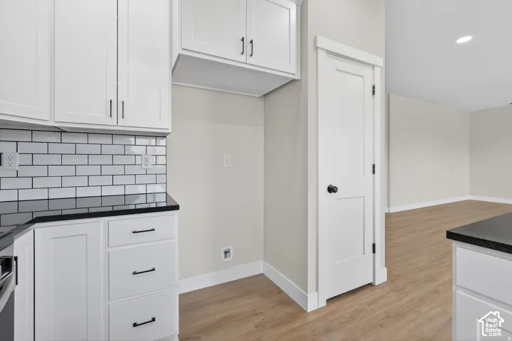 White cabinetry with matte black hardware, subway tile backsplash, dark countertops, wood-finish flooring, and white interior doors