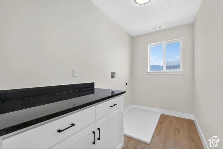 White cabinetry with black hardware, dark stone countertop, wood-finish flooring, and a single window
