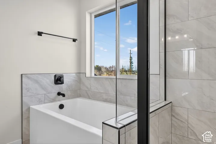 Tiled bathtub with matte black fixtures, framed window, and glass shower enclosure with dark trim