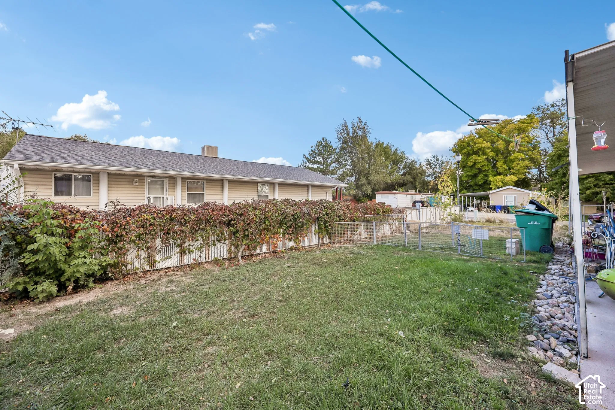Expansive grassy yard with established perimeter plantings, chain-link fencing, and a concrete patio