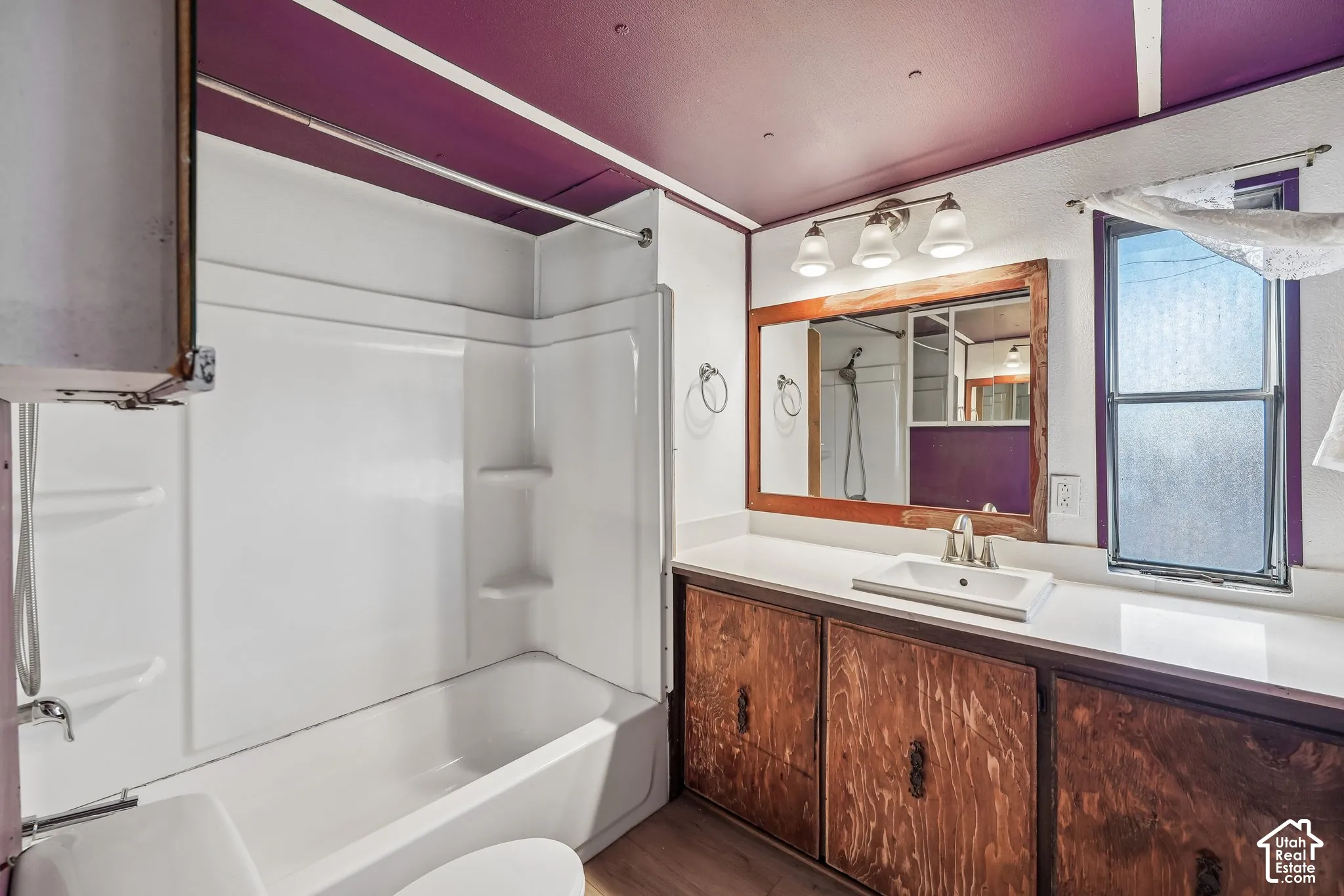 Bathroom featuring a single-piece bathtub/shower combination, wood-finish vanity with an integrated sink, and a wall-mounted vanity light fixture