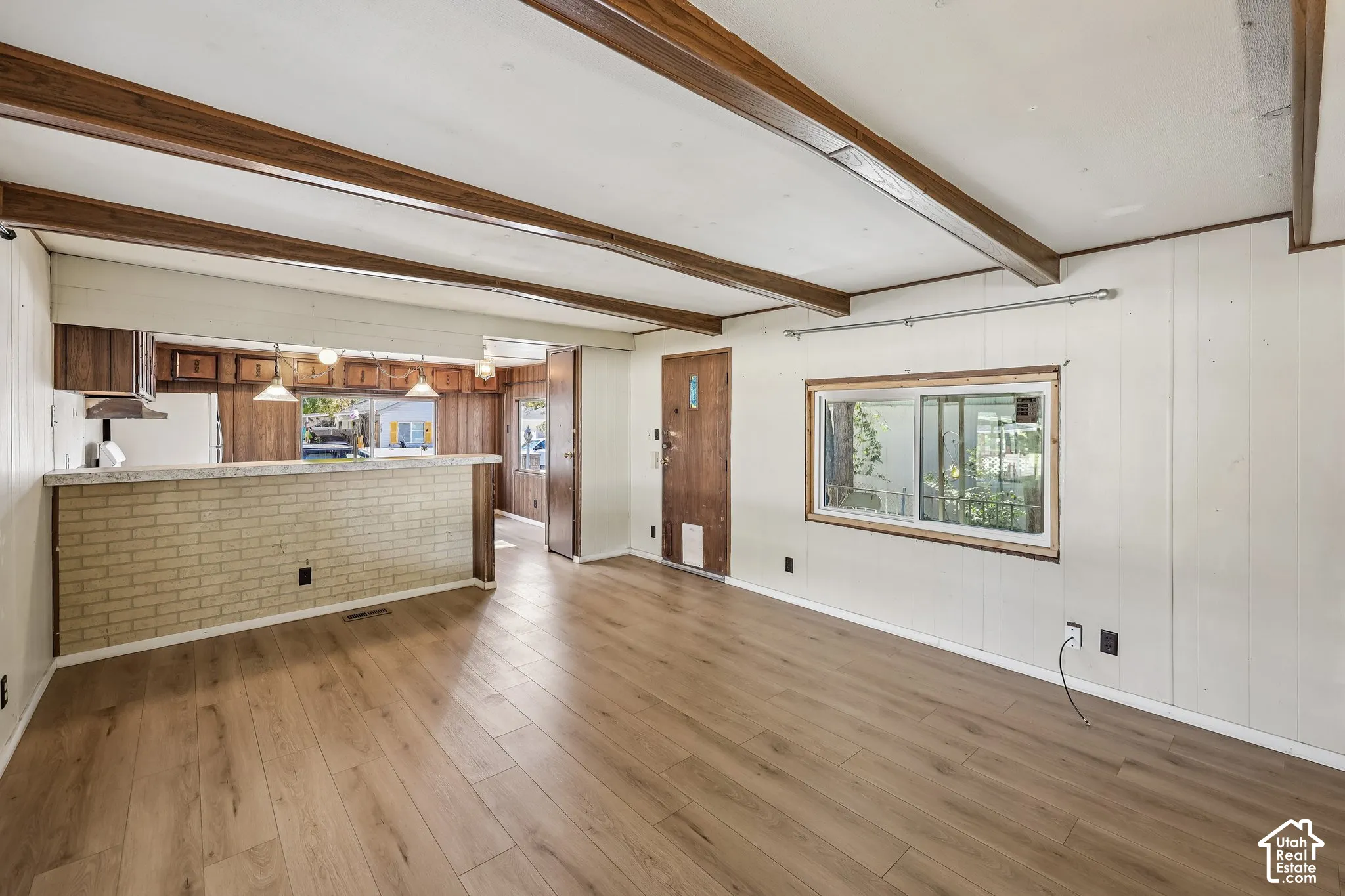 Wood-finish flooring, exposed wood beams, and a light brick-finish breakfast bar with pendant lighting