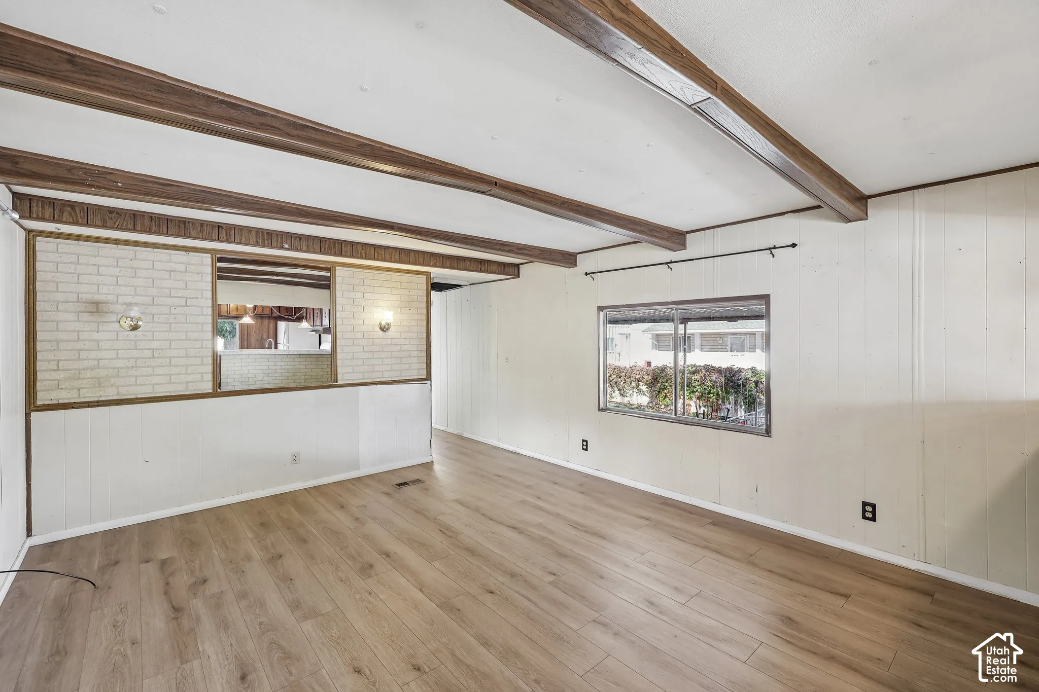 Wood-finish flooring, exposed ceiling beams, and a white brick half-wall with integrated lighting