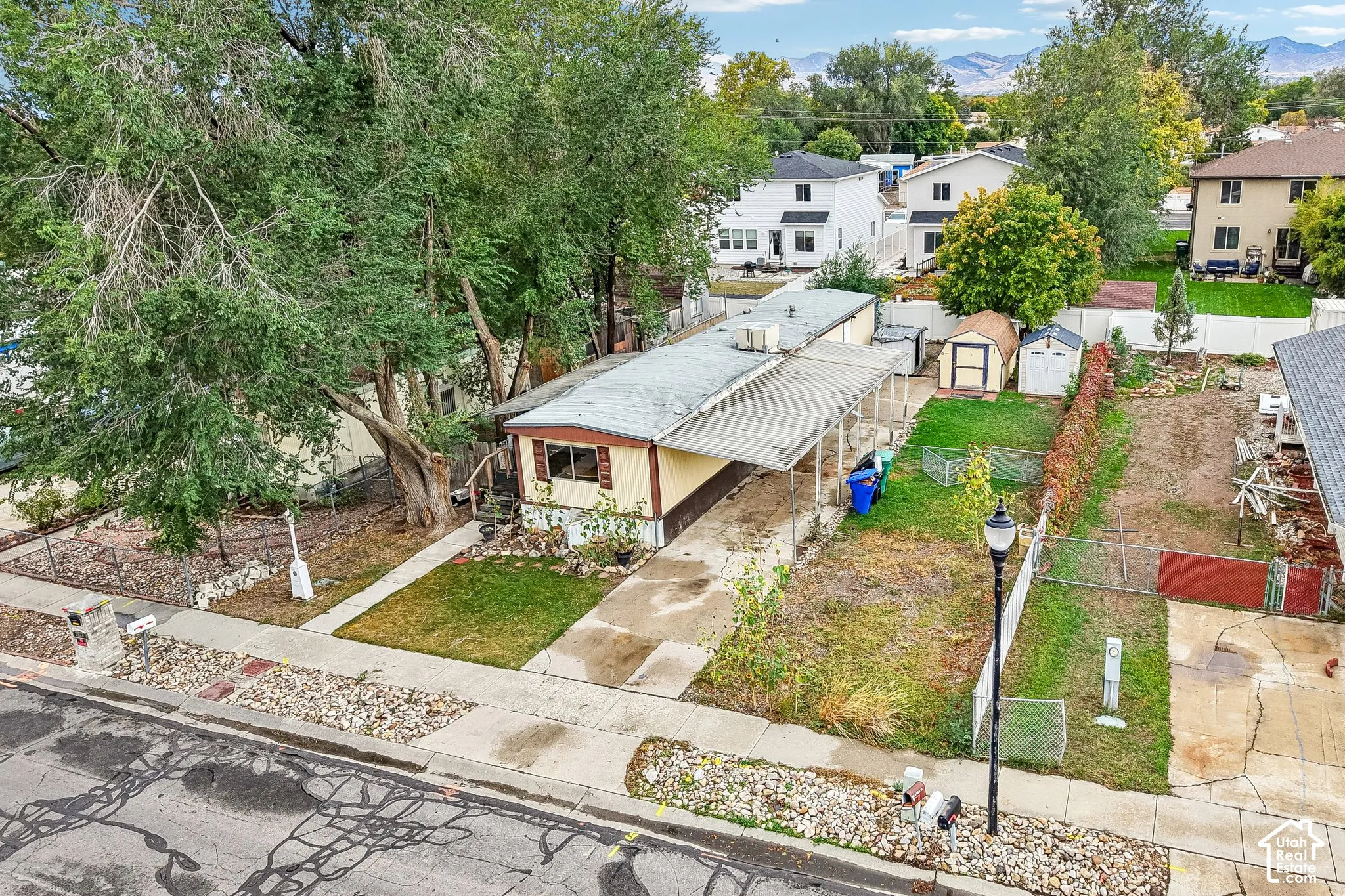 Extended driveway, fenced perimeter, multiple storage sheds, and mature landscaping