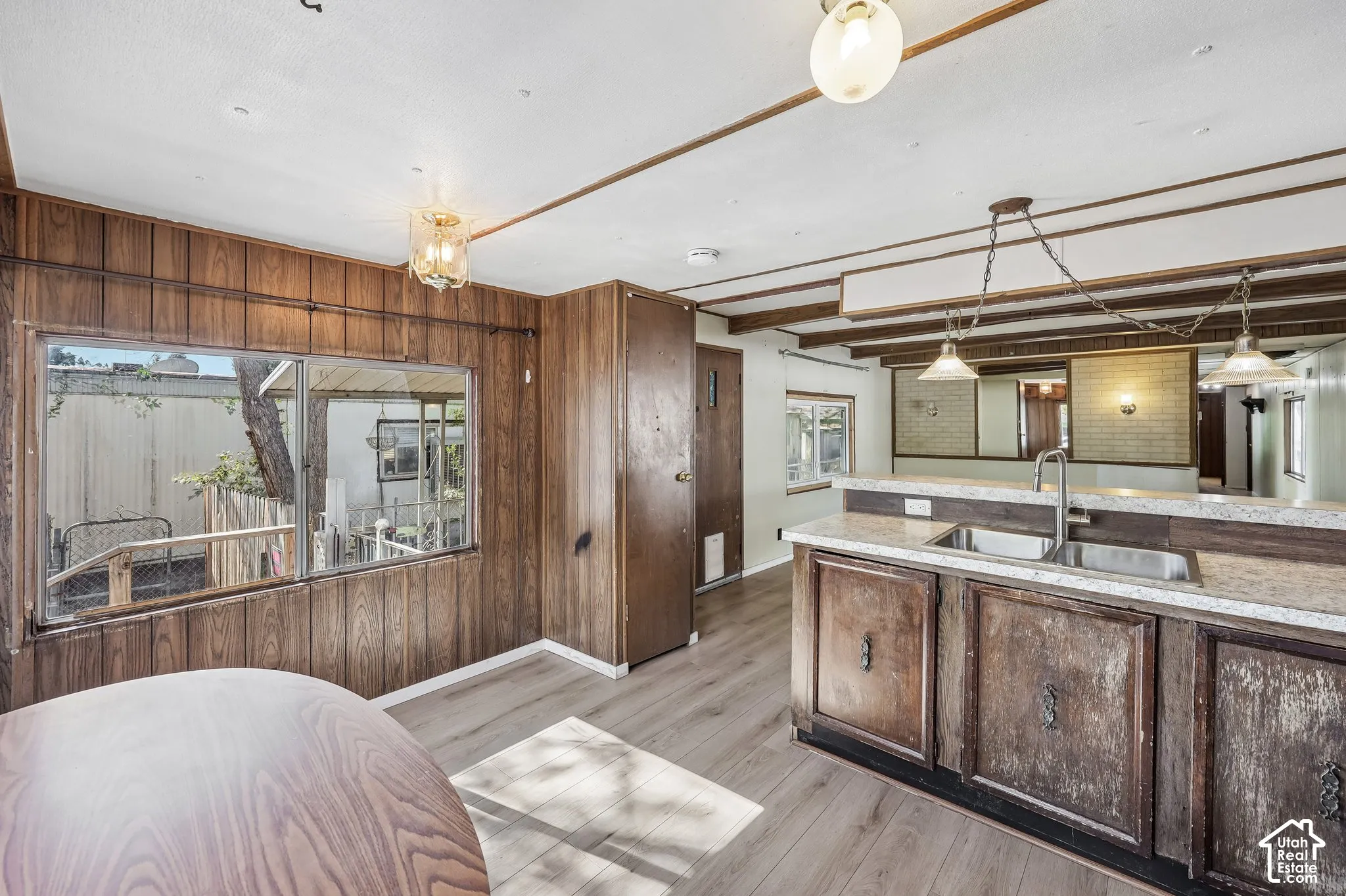 Wood-finish flooring, wood paneling, ceiling beams, and a kitchen island with integrated sink