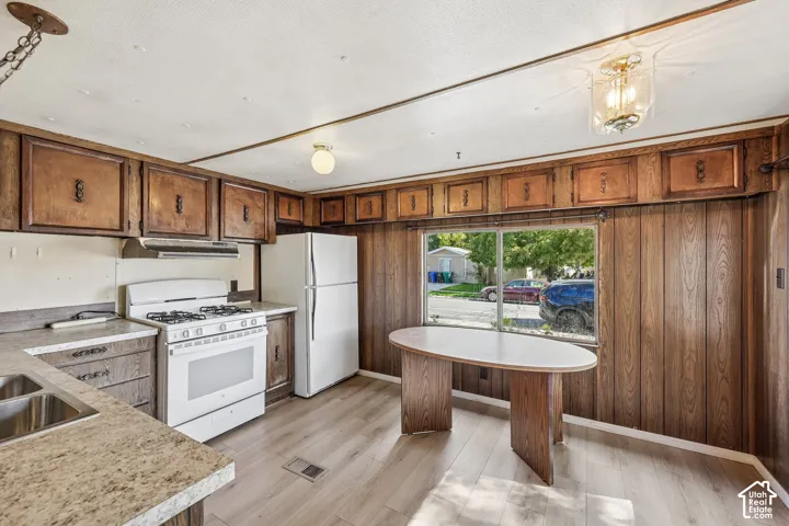 Kitchen with wood-finish cabinetry, white appliances, and light wood-finish flooring