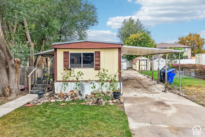 Single-story residence featuring light yellow siding with brown trim, covered front entry porch with wood steps, wood-finish window shutters, an extended carport, and a concrete driveway