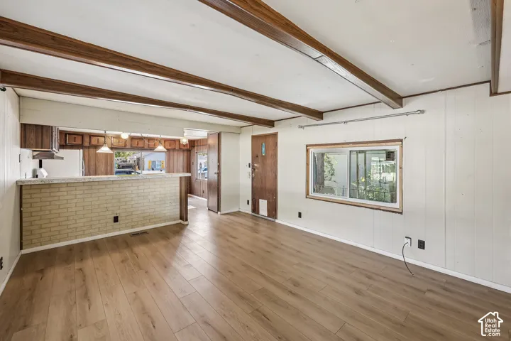 Wood-finish flooring, exposed wood beams, and a light brick-finish breakfast bar with pendant lighting