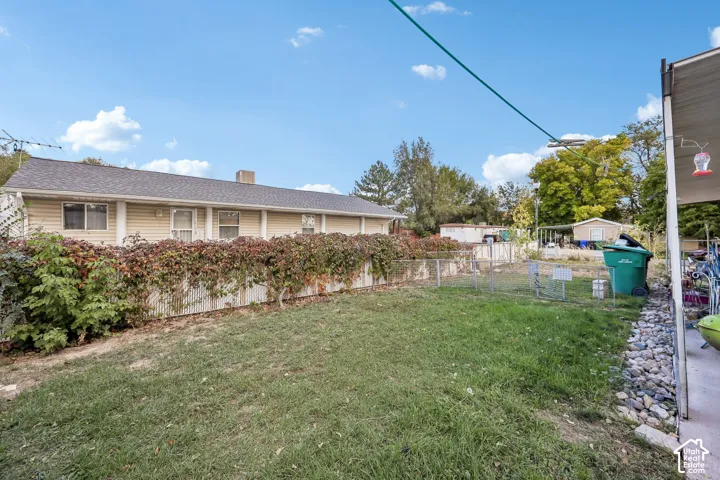 Expansive grassy yard with established perimeter plantings, chain-link fencing, and a concrete patio