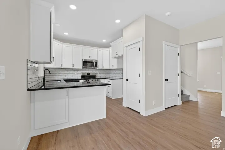Kitchen featuring white shaker cabinetry, stainless steel appliances, black countertops, a subway tile backsplash, and wood-finish flooring