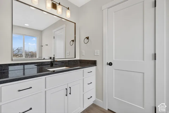 White wood-finish vanity with drawer and cabinet storage, dark stone countertop, undermount sink, and black-finish faucet