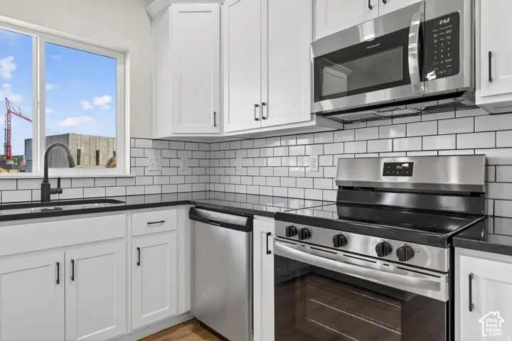 White shaker-style cabinetry with matte black hardware, stainless steel appliances, a subway tile backsplash, a black countertop, and a stainless steel sink with a black faucet