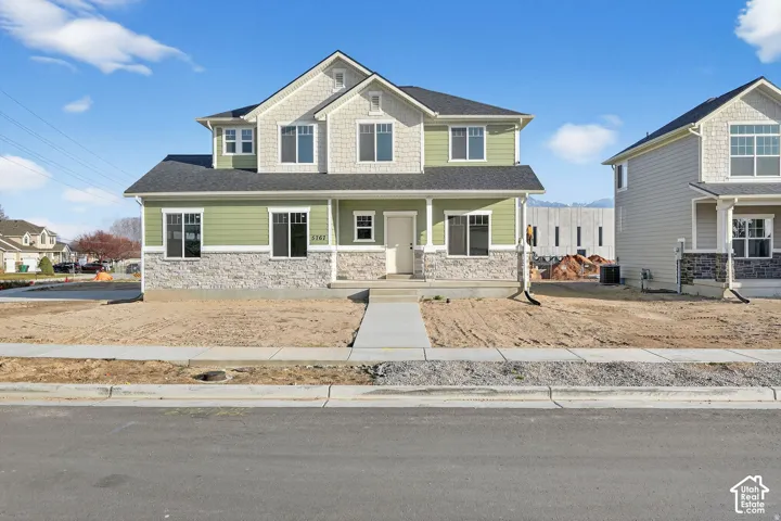 Two-story residence with a green and gray exterior, stone facade detailing, and a prominent front entrance