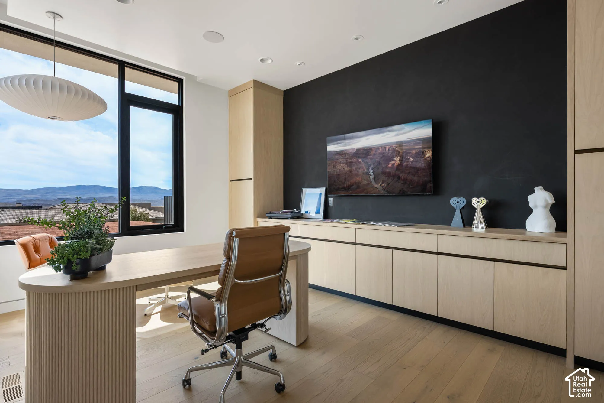 Hardwood-style flooring, large windows, mountain scenery, light wood-finish built-in cabinetry, and a black accent wall