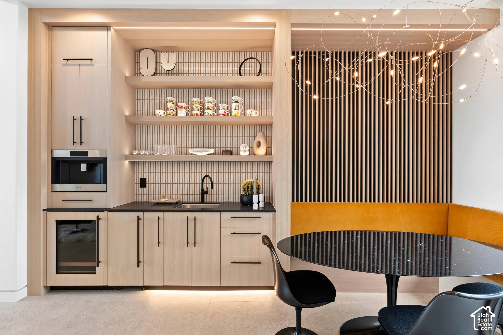 Custom built-in cabinetry with integrated coffee maker and beverage refrigerator, open shelving with accent lighting, dark countertop with undermount sink, and slat wall paneling