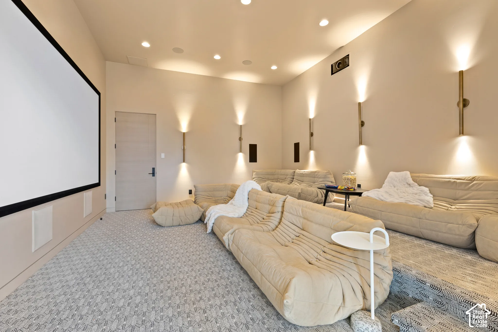 Dedicated media room featuring a large projection screen, recessed ceiling lighting, and layered patterned carpeting