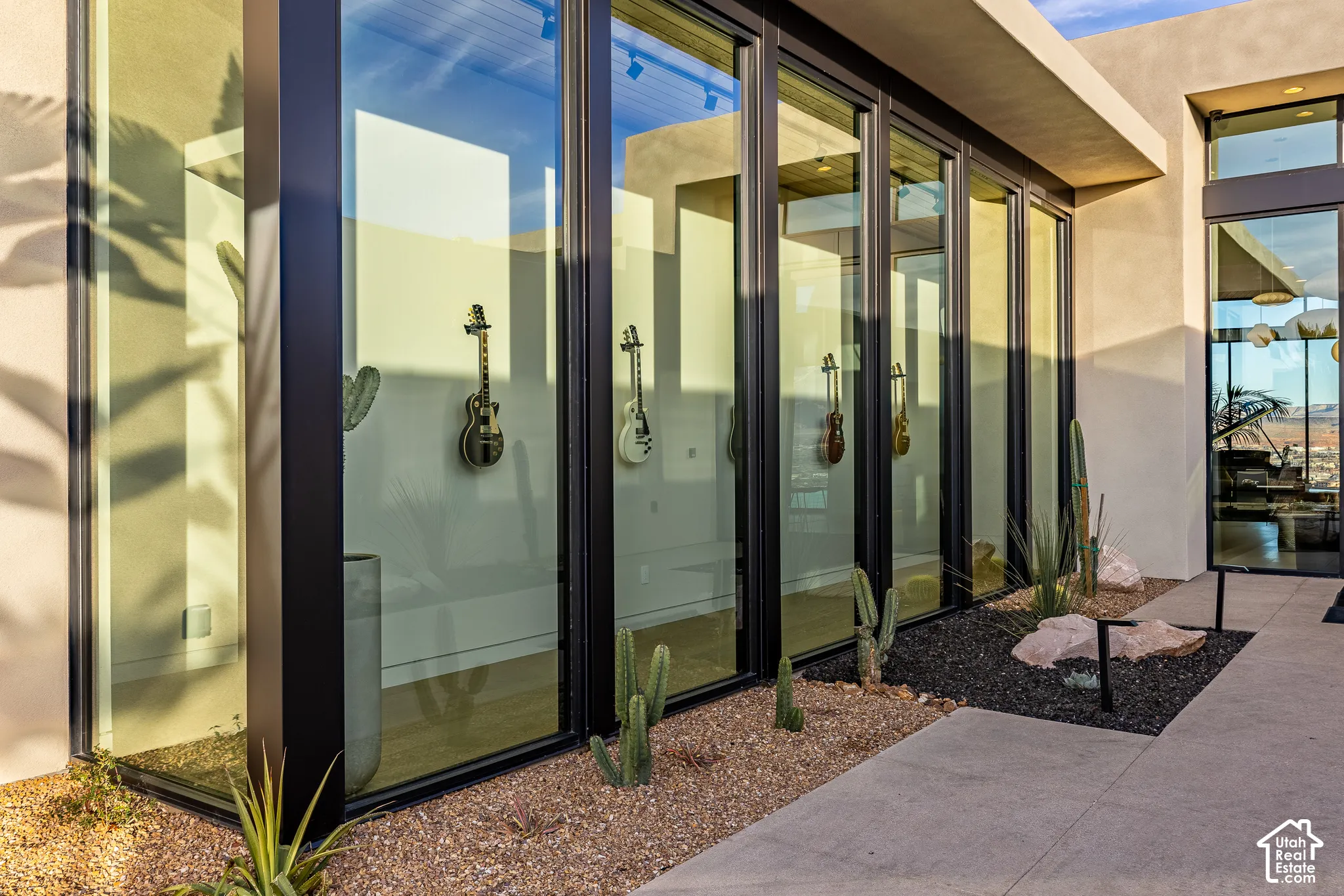 Expansive floor-to-ceiling windows with black frames, concrete exterior, and a desert landscape with gravel and natural rock elements