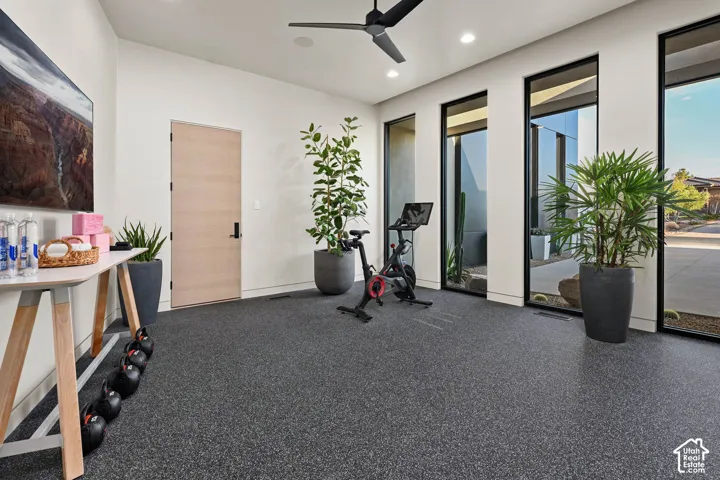 High ceilings with recessed lighting, dark finish ceiling fan, full-height windows with dark frames, light wood-finish door, and speckled resilient flooring