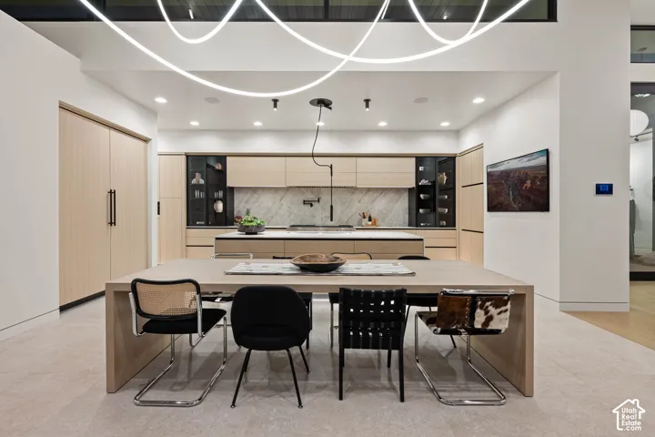 High ceilings with linear suspended lighting, wood-finish cabinetry, a large kitchen island with counter seating, integrated appliances, and a full-height stone slab backsplash