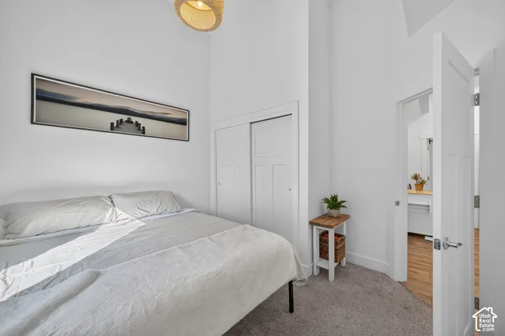 White walls, high ceilings, carpet flooring, sliding closet doors, and a door leading to an additional space with wood-finish flooring