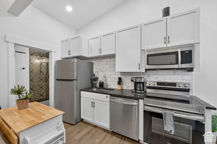 Compact kitchen featuring stainless steel appliances, white shaker-style cabinetry, dark stone countertops, and a white subway tile backsplash