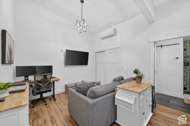 Vaulted ceiling with an exposed beam, wood-finish flooring, modern chandelier, wall-mounted air conditioning unit, and a sliding barn door