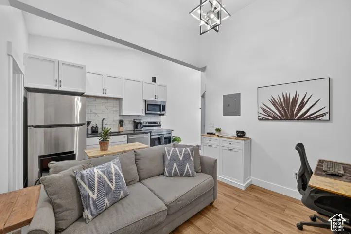 Hardwood-style flooring, stainless steel appliances, white cabinetry with dark hardware, tiled kitchen backsplash, and a contemporary ceiling light fixture