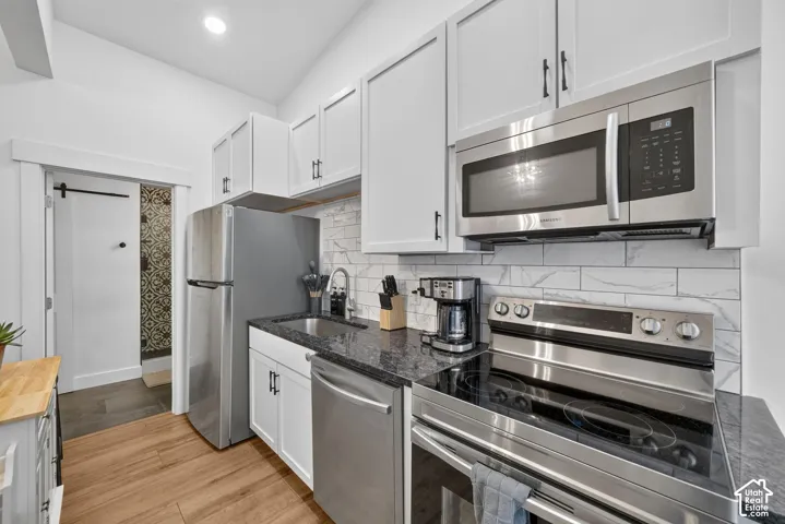White shaker cabinetry, stainless steel appliances, dark stone countertops, wood-finish flooring, and subway tile backsplash