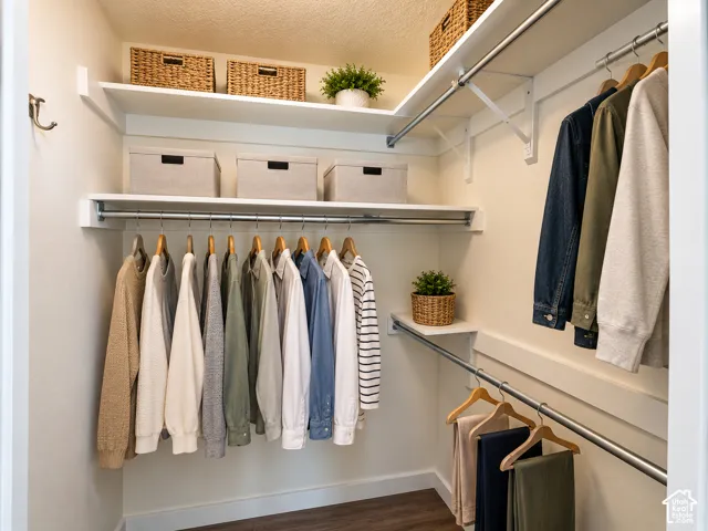 Walk-in closet featuring multi-level metal garment rods, fixed wood shelving, and wood-finish flooring