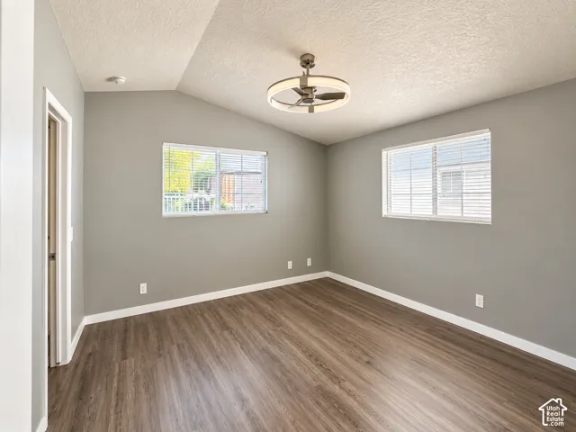 Room featuring vaulted ceilings, wood-finish flooring, two dual-pane windows with horizontal blinds, and a circular LED ceiling fan fixture