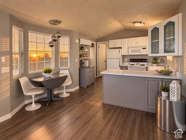 Kitchen area featuring wood-finish flooring, white cabinetry with glass-panel accents, peninsula with solid-surface countertops, and multi-light pendant fixture