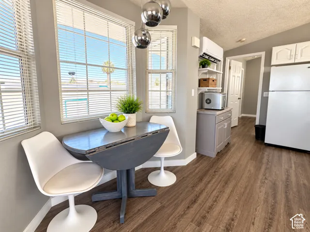 Bay window with natural lighting, wood-finish flooring, multi-globe pendant light fixture, wall-mounted climate control unit, and built-in lower cabinetry