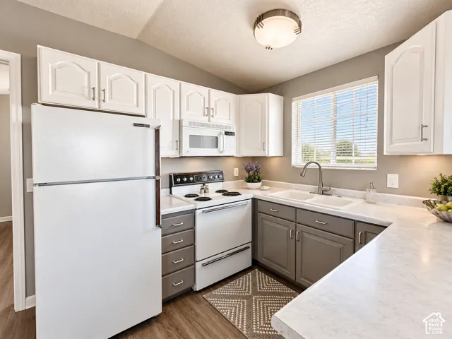 Kitchen featuring two-tone cabinetry, white laminate countertops, a double-basin sink, an over-the-range microwave, and wood-finish flooring