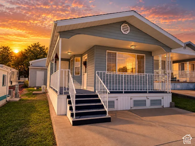 Exterior featuring light blue horizontal siding, a covered porch with white metal railings, wide-paned windows, and a concrete driveway