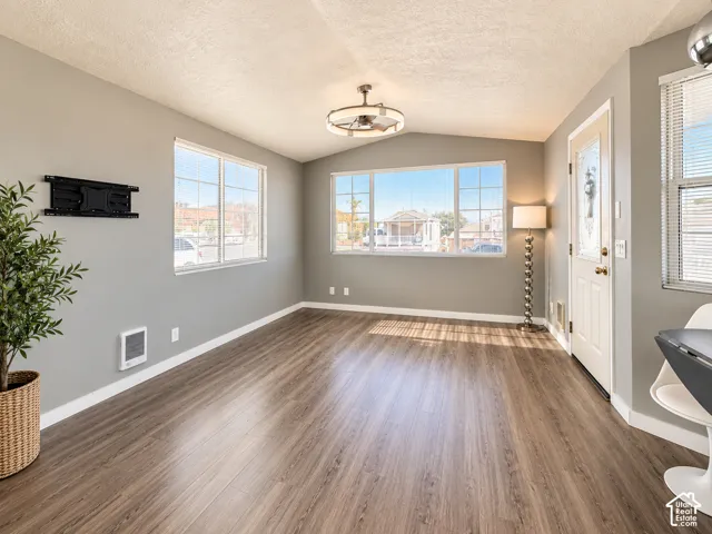 Living area featuring wood-finish flooring, large windows with natural light, vaulted ceilings, a modern industrial-style drum chandelier, and an exterior door with decorative glass inlay