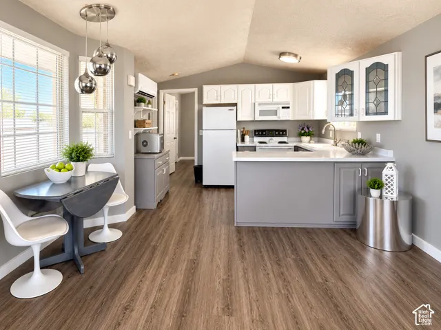 Kitchen featuring wood-finish flooring, white cabinetry with glass-panel inserts, a peninsula with a solid-surface countertop, and a multi-light pendant fixture