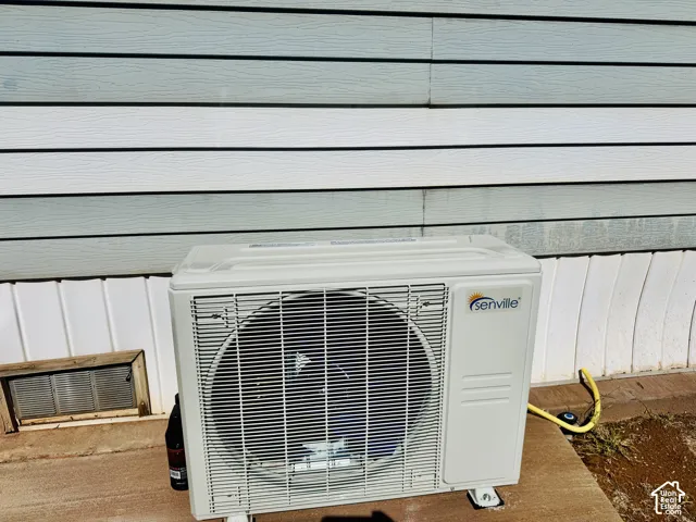 Exterior HVAC condenser unit mounted on a concrete pad with light blue horizontal siding