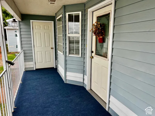 Covered porch with blue carpeting, light blue siding, and white railing